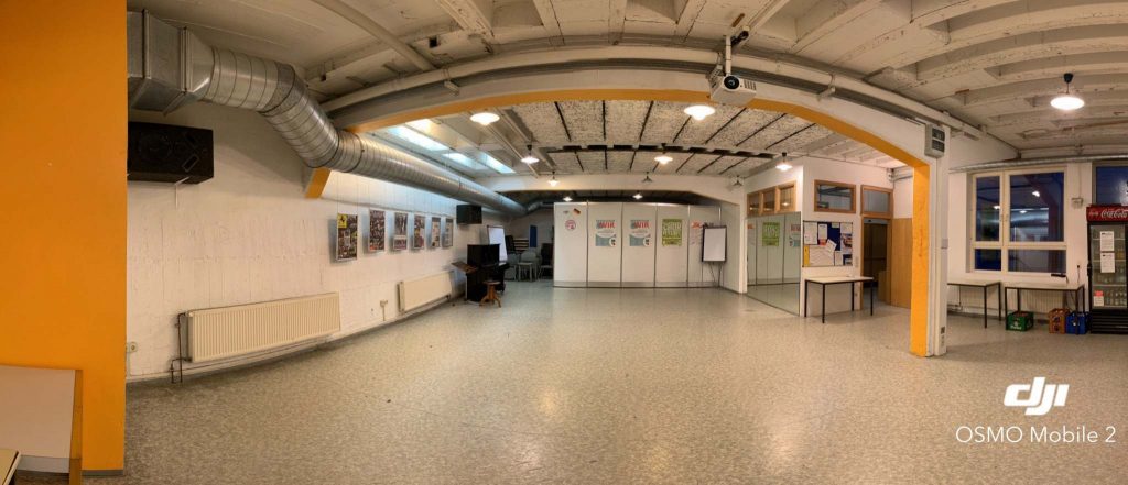 Blick auf einen großen, leeren Raum. Rechts stehen drei Tische sowie ein Getränkekühlschrank.